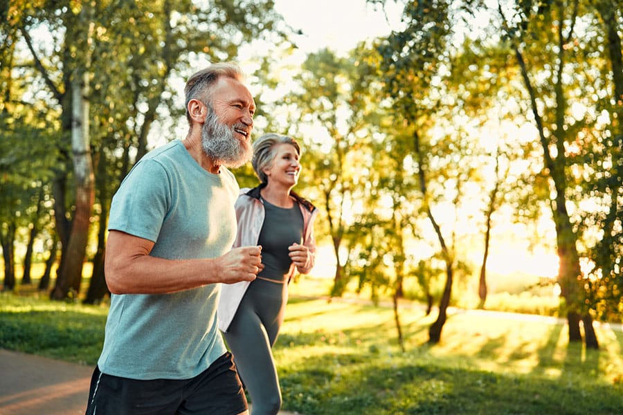 A smiling older man and woman jog together on a path in a sunlit Warren MI park, surrounded by green trees and warm sunlight filtering through the leaves, enjoying the benefits of shoulder pain treatment. A smiling older man and woman jog together on a path in a sunlit Warren MI park, surrounded by green trees and warm sunlight filtering through the leaves, enjoying the benefits of shoulder pain treatment.