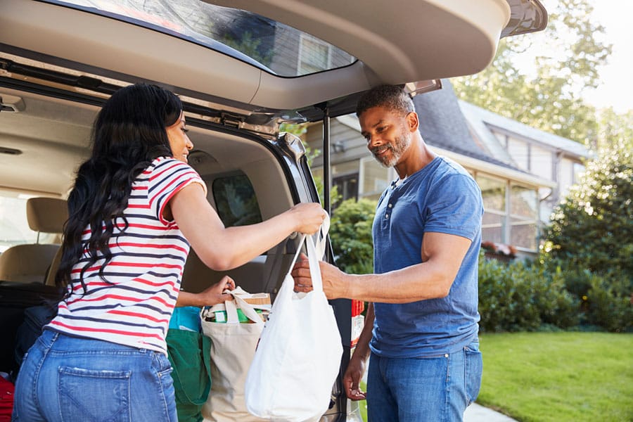 A woman and a man load groceries into the back of an SUV parked outside a house on a sunny day, moving beyond the challenges that joint degeneration or osteoarthritis can bring.